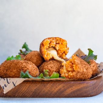 Rice balls stuffed with mozzarella cheese and deep fried on a wooden plate. Light background.